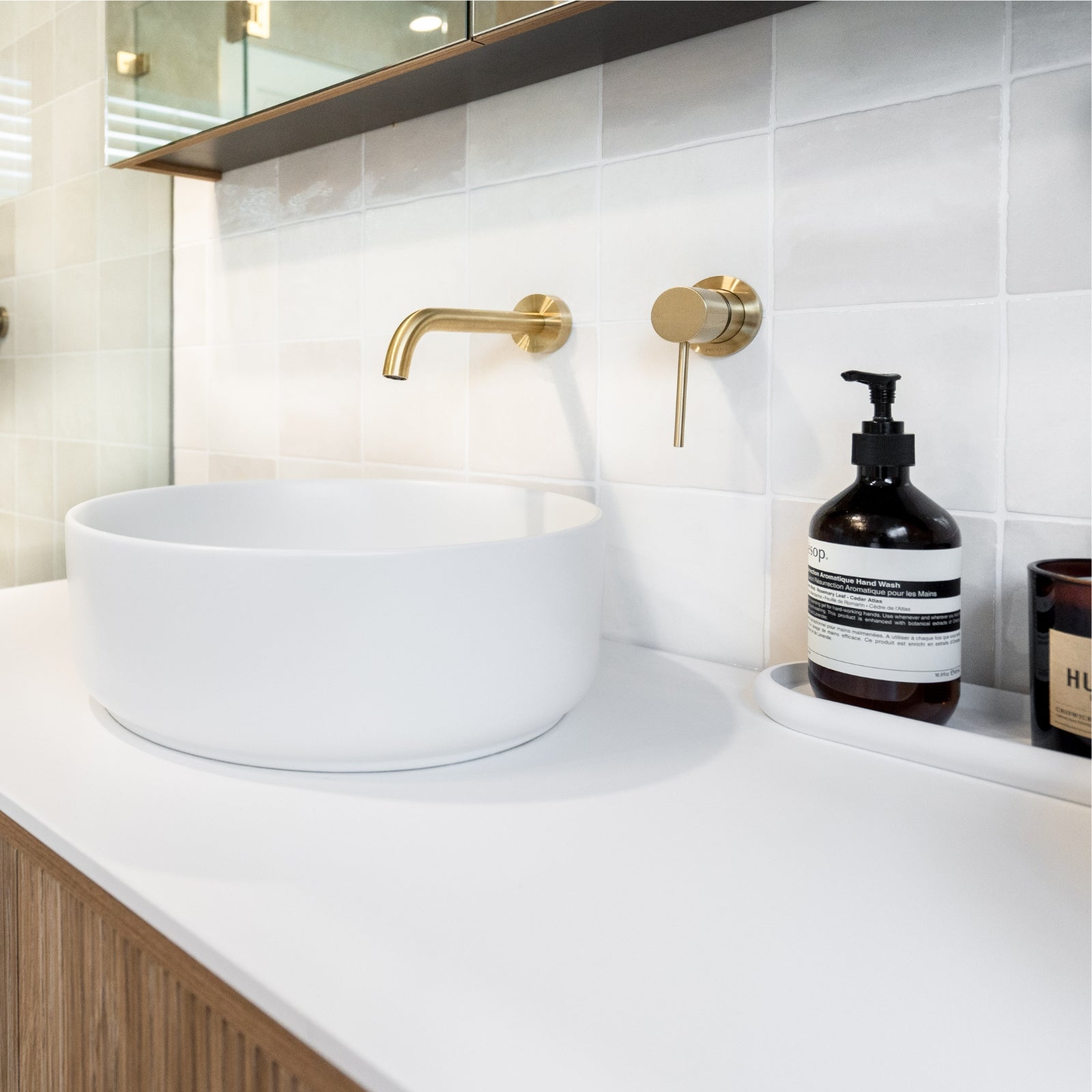 Bathroom vanity with white sink, gold faucet, and a bottle of soap on a white countertop. Snow White Ella Zellige Tile 100 x 100 x 10mm Spanish Ceramic | The Blue Space