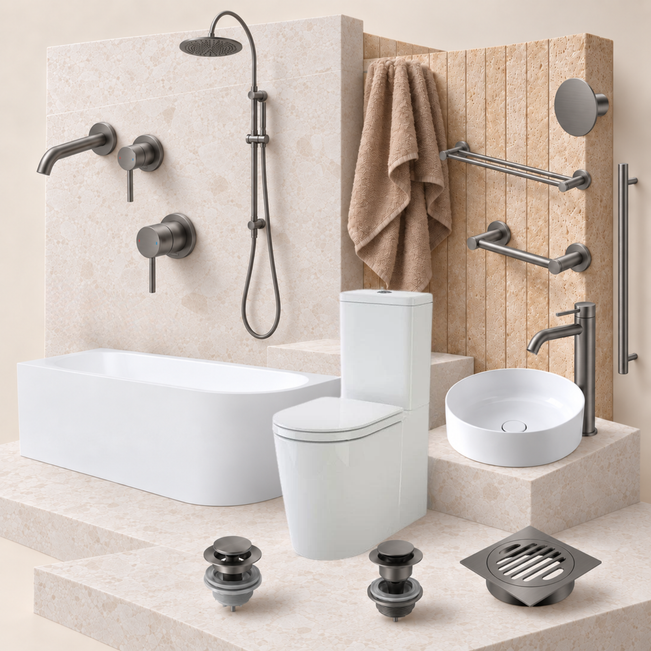 A coordinated bathroom fixture set displayed on a staged bathroom set: a white freestanding bathtub, white toilet, white vessel sink, matte dark metal shower system, drain, floor drains, towel rack, and wall-mounted hardware. The background is a warm beige stone wall and platform.
