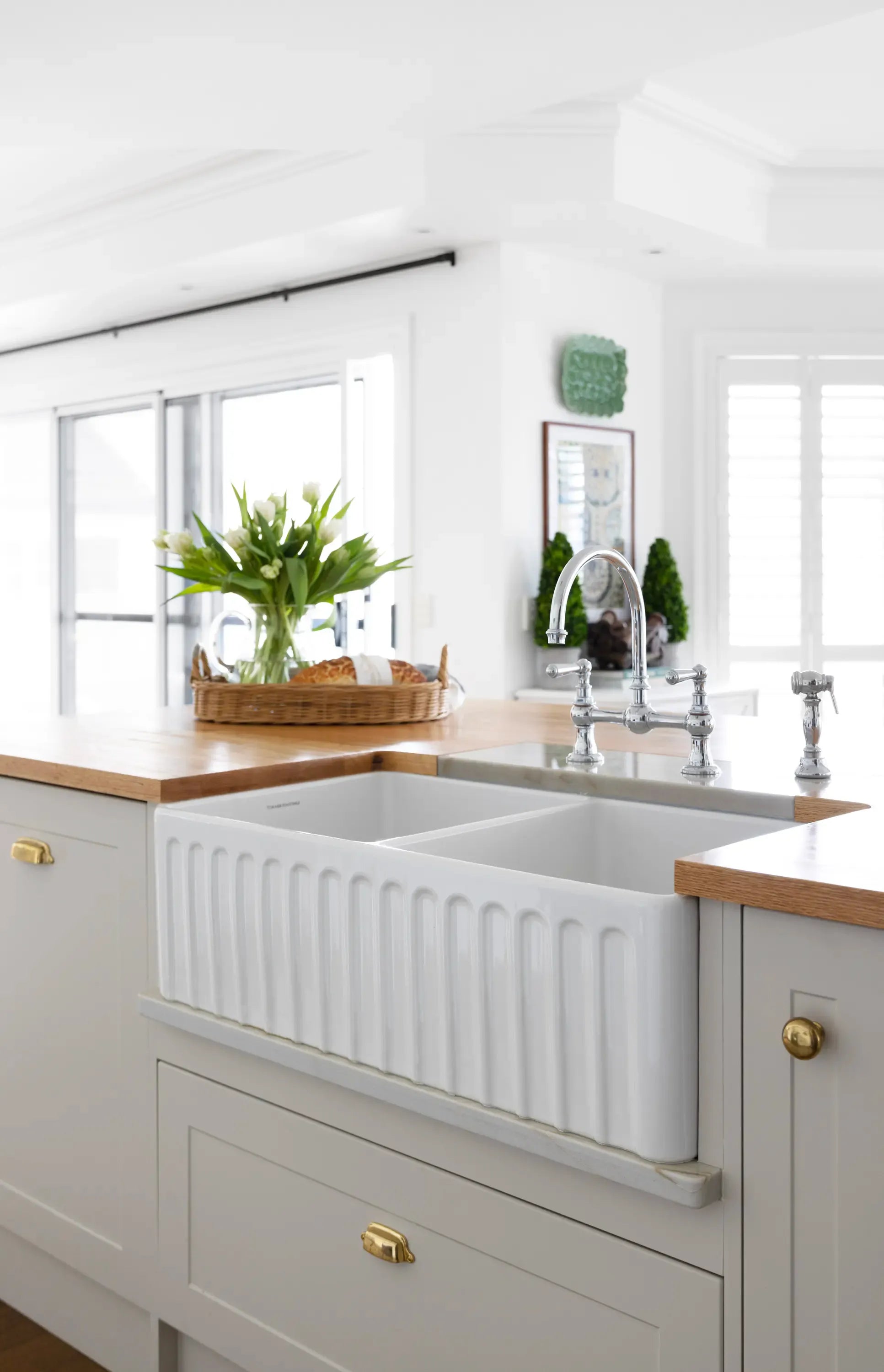 White farmhouse sink in a kitchen with wooden countertops and light gray cabinets.