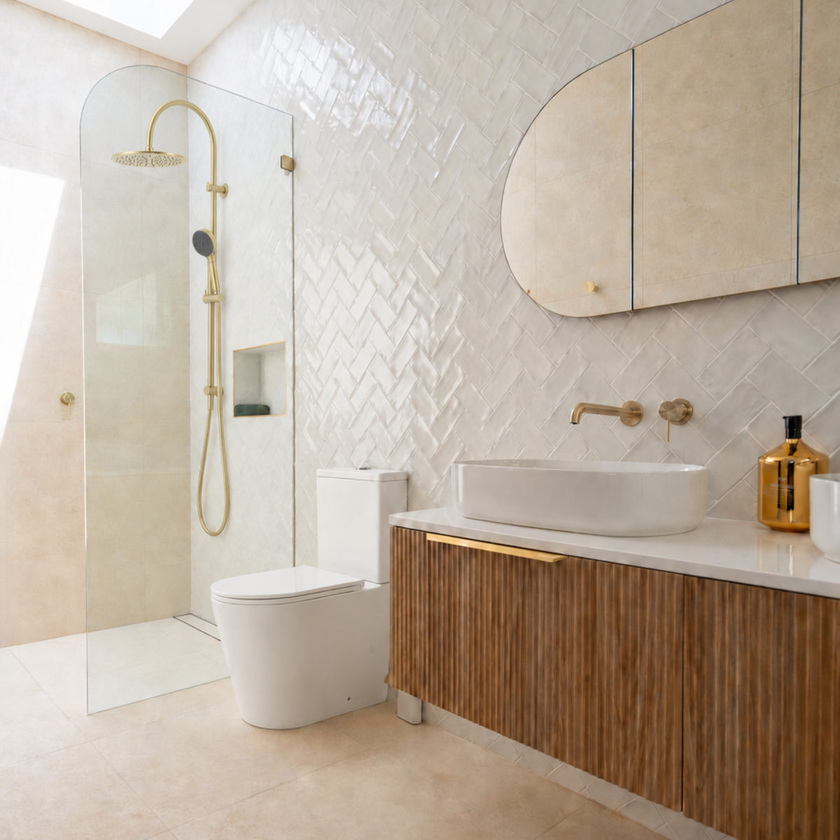 A modern bathroom interior featuring a walk-in shower with a glass door, white toilet, vessel sink on a wood-look vanity, and a large arched mirror against a beige tiled wall.
